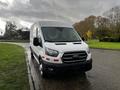 A 2020 Ford Transit van with a white exterior and red reflective stripes parked on a wet road