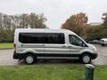 A 2019 Ford Transit van in silver parked on a grassy area with large windows and black accents