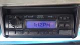 A car stereo displaying the time 1:12 PM with various buttons and knobs for audio settings and features