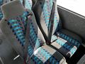 Two gray bus seats with blue and teal patterned upholstery, each featuring a seatbelt securely fastened across the seatback