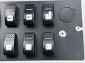 A panel featuring six black control switches labeled with icons for various functions on a 2015 Spartan School Bus