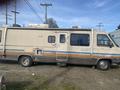 A 1987 Chevrolet Fleetwood Pace Arrow motorhome with a beige exterior and blue stripes featuring a side entrance door and various windows