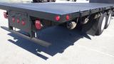 A black 2017 Freightliner M2 106 flatbed truck with a textured bed surface and red tail lights visible on the rear end