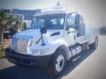 A white 2011 International DuraStar 4300 truck with a flatbed and tool compartments on the side