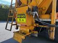 A yellow warning sign on a piece of machinery indicates "KEEP BACK 15 m" attached to the rear of a truck with hydraulic hoses and a metal chute
