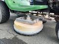 A close-up of the underside of a 2021 John Deere L Series S riding mower showing the mowing deck with a circular blade and brushes