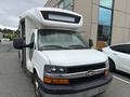 A white 2017 Chevrolet Express with a large front cab and prominent Chevrolet logo on the grille parked in front of a building