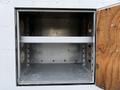 An empty storage compartment with a metal interior featuring two circular openings on the sides and a horizontal metal shelf in the middle