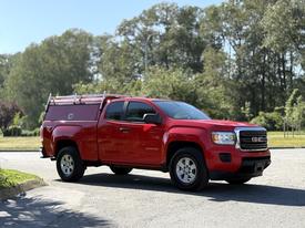 A red 2018 GMC Canyon pickup truck with a fitted bed cover parked on a road