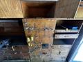 A wooden storage unit with multiple drawers hooks and various tools attached it features a worn surface with visible scratches and markings