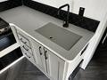 Grey countertop with a built-in sink and modern black faucet alongside white cabinets with black handles