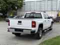 A white 2016 GMC Sierra 1500 pickup truck with a chrome rear bumper and a bed cover viewed from the rear angle
