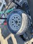 A 2015 Snake Trailer wheel with a metal rim and tire showing tread patterns placed on a trailer frame