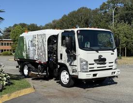 A 2014 Isuzu NRR street sweeper truck with a distinct white and green design and a rotary brush at the front