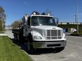 A 2012 Freightliner M2 112 truck with a flatbed and various tools and equipment mounted on the rear with orange warning lights on the roof