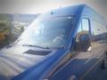 A blue 2017 Mercedes-Benz Sprinter van with a large windshield and sleek design is shown in the foreground