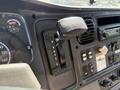 Close-up of the gear shift lever of a 2015 Freightliner M2 106 showing the positions R N D 3 2 L and various control buttons and gauges on the dashboard