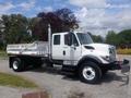 A white 2012 International 7300 truck with a flatbed and exhaust stack, featuring orange lights and safety markers on the side