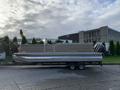 A 2013 Sylvan 13-person pontoon boat on a trailer with a silver and gray exterior and a motor mounted at the rear