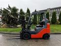 A 2017 Toyota 8FCGCU25 forklift with a red and gray body features two long forks and an enclosed operator compartment