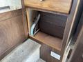 An open cabinet with a wooden door revealing a small compartment containing a light green hose and an electrical outlet on the side