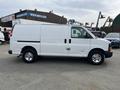 A white 2013 Chevrolet Express van parked with its side facing the viewer showcasing its sliding door and chrome wheels