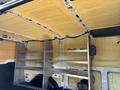 Interior of a 2016 Ford Transit van featuring insulation on the walls and a metal shelving unit installed on one side