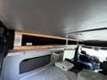 Interior of a 2017 Mercedes-Benz Sprinter showing a wooden storage shelf above a bed area with bedding and a view of the front seats