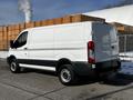 A 2018 Ford Transit van with a white body and black accents parked on a street showing a side view of the vehicle