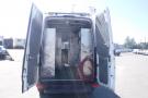 A 2012 Mercedes-Benz Sprinter van with its rear doors open revealing an empty cargo space and some equipment inside