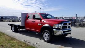 A red 2015 RAM 5500 pickup truck with a flatbed in the foreground facing slightly to the right