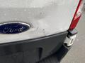 A 2018 Ford Transit with a dent on the rear door and raindrops on the surface showing the blue Ford emblem and part of the tail light