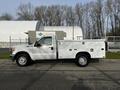 A 2016 Ford F-350 SD in white with a utility bed featuring compartments and a single cab design parked on a concrete surface