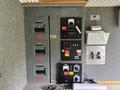 A control panel with multiple circuit breakers switches and gauges mounted on a gray wall