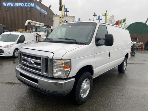 A white 2011 Ford Econoline van with a front grille and large tires parked on wet ground