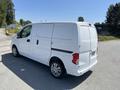 A white 2019 Nissan NV200 cargo van with a sliding side door and rear doors parked on a road