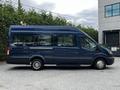 A blue 2017 Ford Transit 350 van with a high roof and large windows parked on a gravel surface, showcasing its side profile and wheels