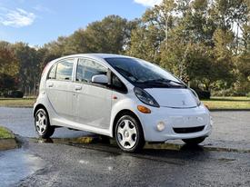 A 2012 Mitsubishi I-MiEV is parked with its compact design visible showcasing a white exterior and five-spoke alloy wheels