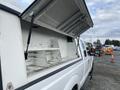 A 2015 Ford F-250 SD with a raised truck bed cap revealing empty shelves inside