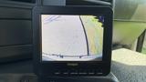 A monitor displaying a rearview camera feed showing the view behind a vehicle with grid lines for parking assistance