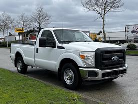 A white 2011 Ford F-250 Super Duty pickup truck with a black grille and chrome bumpers is parked on the side of the road facing forward