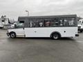 A side view of a 2018 Chevrolet Express bus with a white body and gray roof featuring large windows along the passenger area