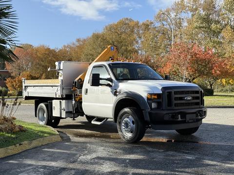 A white 2008 Ford F-550 with a flatbed and mounted crane is parked on a paved surface in a well-maintained area