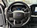 A close-up view of the steering wheel of a 2021 Ford F-150 featuring buttons for audio and cruise control with the Ford logo prominently displayed in the center