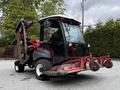 A 2012 Toro Groundsmaster with a black and red exterior features a cab, steering wheel, and elevated mower deck at the rear with multiple cutting blades visible