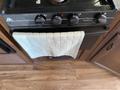 A black gas stove with four knobs and a green dish towel hanging from the front