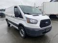 A white 2018 Ford Transit van is parked with a slightly wet surface and features a black grille with rounded headlights and sliding side doors