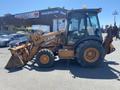 A 2008 Case Super 580M tractor with a yellow and brown exterior, equipped with a front loader and backhoe attachment, positioned for operation