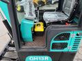 A 2024 AGT Industrial Green QH13R Mini Excavator featuring a seat with protective covering a control panel with levers and a bright yellow control box next to it