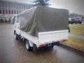 A white 2003 Toyota Toyoace truck with a gray tarpaulin cover on the cargo bed parked on the street